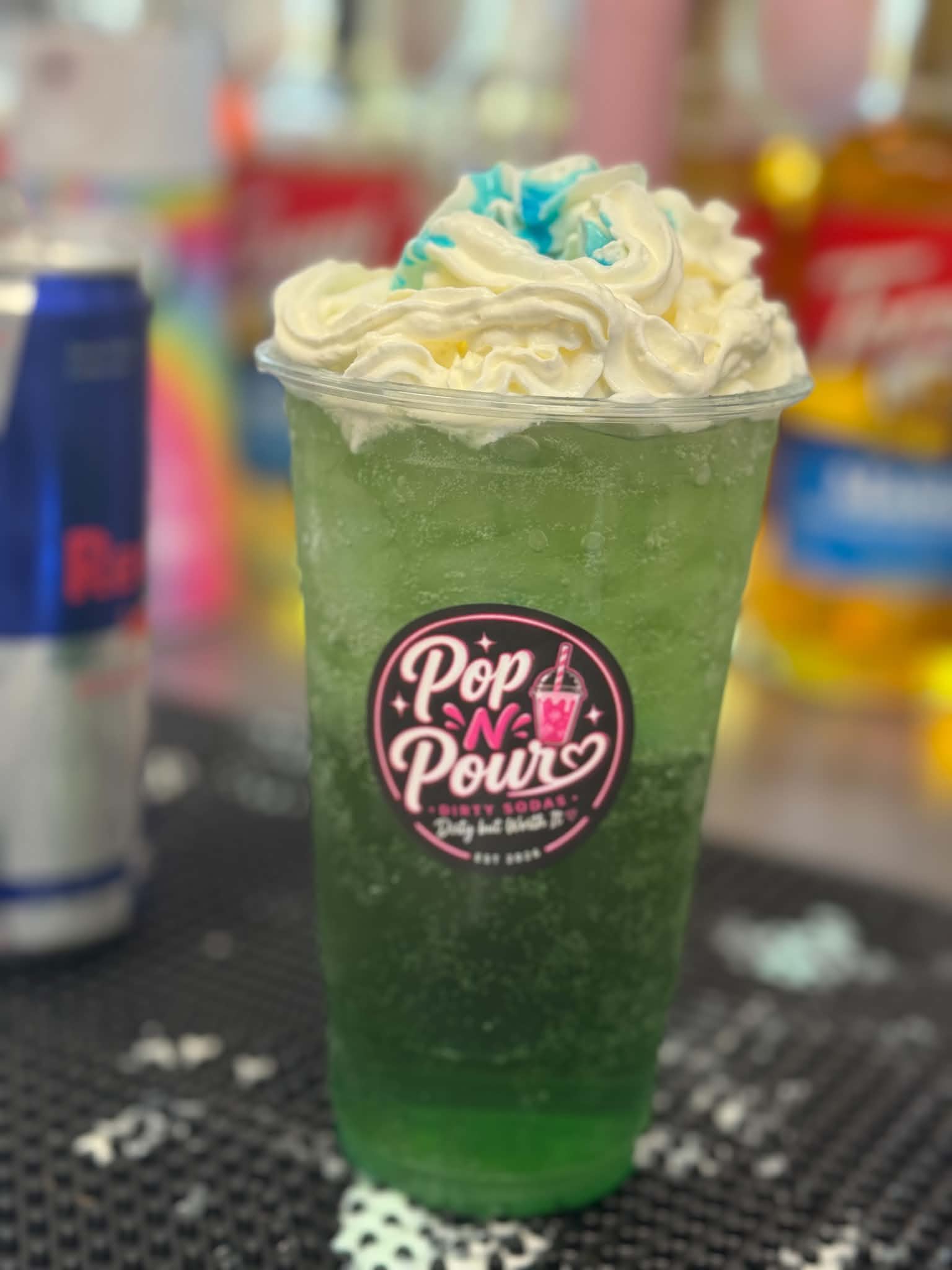 A green Pop N Pour soda topped with whipped cream and blue sprinkles